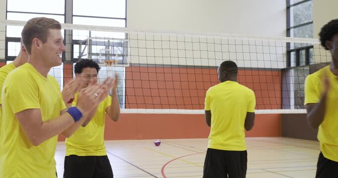 Diverse male volleyball team in yellow tees huddling stacking chanting embracing at net after point