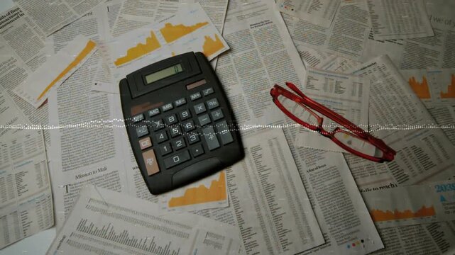 Black calculator sitting on tabletop with yellow charts red glasses sliding right, waveform moving