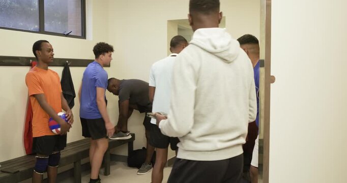 Diverse male team watching hoodie man entering locker room, giving pep talk, holding volleyball