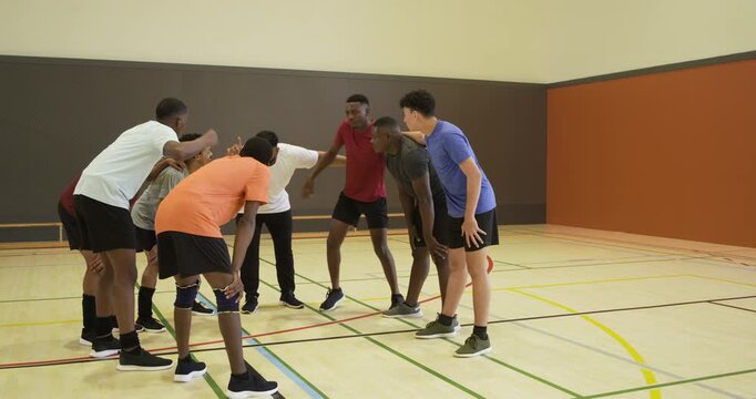Diverse male team gathering center court, volleyball being placed, white-shirt leader giving pep