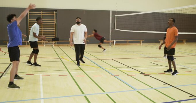 Male teammates reacting to low fast ball, diving, passing volleyball over net, keeping rally in gym