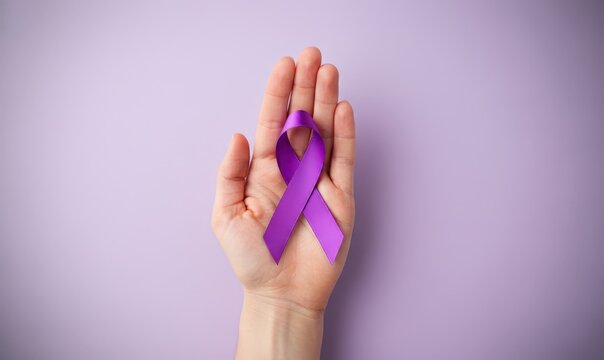 Testicular Cancer Awareness Month concept. Hand of woman holding purple ribbon on pastel lilac background. Symbolic for Pancreatic Cancer in November, Purple Day of Epilepsy, Lupus, Sarcoidosis.