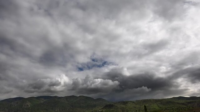 Timelapse of storm clouds gathering above mountain ridges, dark overcast sky thickens fast. Rapid cloudbank builds over highlands as thermal convection drives moisture into condensation layers.