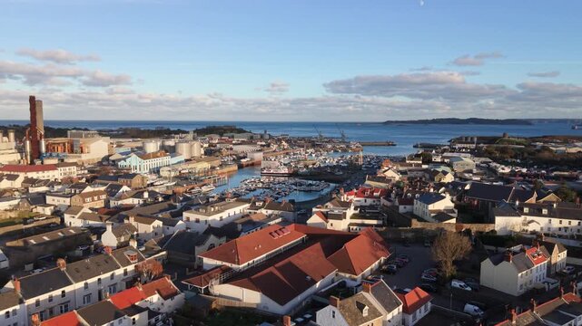 St Sampson Guernsey high reveal over the rooftops of St Sampson past power station,over the Coop and backwards in golden afternoon sun with Vale Castleand Herm in the background