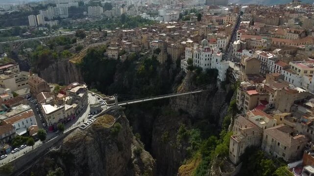 Cinematic aerial view of the Sidi M'Cid suspension bridge crossing the deep Rhumel River gorge in the historic city of Constantine, Algeria.