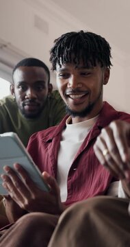 Friends, tablet and watch sport in living room with chat, bonding together and football entertainment. Low angle, people and discussion in home with tech, live stream or soccer game on weekend break.