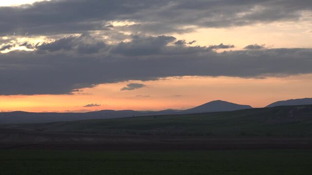 Sunset sky over Chad Niger border, dramatic clouds above dark Sahel plains horizon. Dusk glow lights remote desert foothills, amber afterglow behind layered stormbank silhouettes.