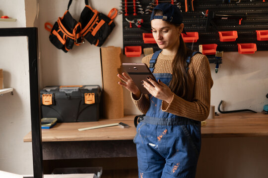 Female worker in overalls using digital tablet in workshop planning small business startup