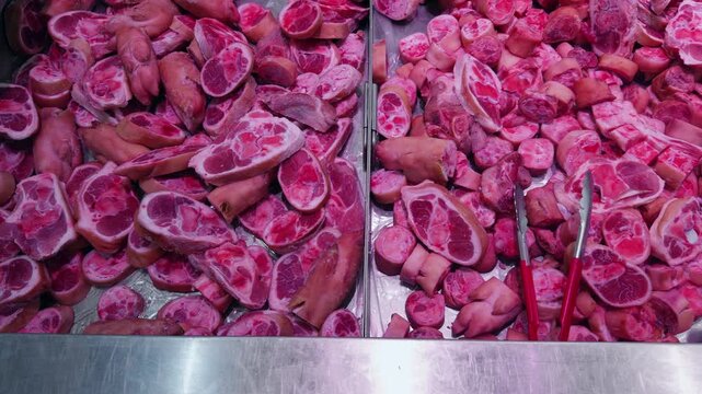 Assorted Raw Bone Cuts and Meat Pieces Displayed in Metal Counter at Butcher Shop Market. Fresh Animal Products Prepared for Cooking and Sale
