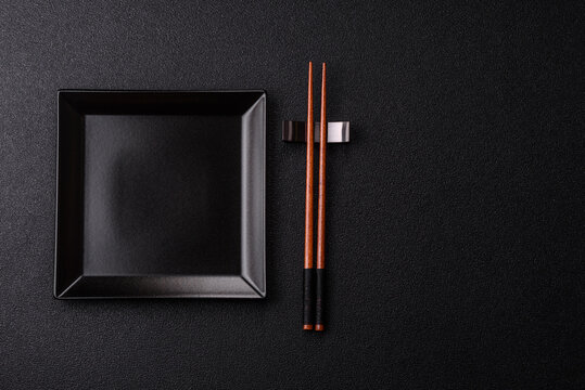 An empty ceramic square black plate with chopsticks for Asian food. An empty square plate