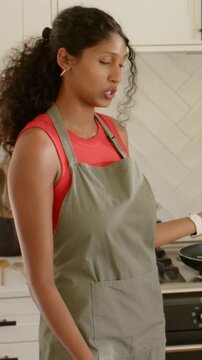 Vertical video: Reaching pan, cook in green apron stirring on gas stove, demonstrating recipe