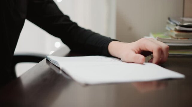 Child reaches quickly for pen on desk. Young boy extends arm to grasp writing instrument carefully. Grandson swiftly reaches across his desk to grab pen during focused study session
