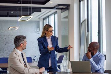 Obraz premium Businesswoman leading a team meeting, presenting ideas and discussing strategy with diverse colleagues in a corporate office environment