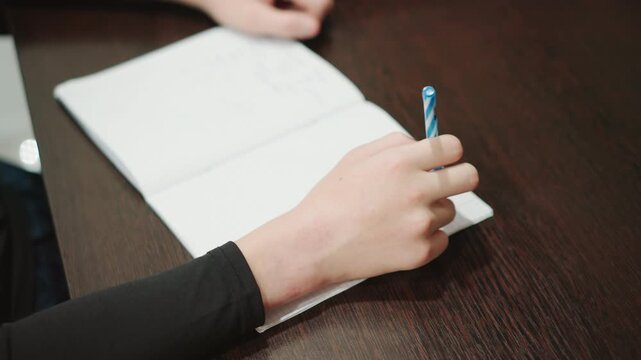 Focused youthful writing. Teen studying with neat handwriting. Individual concentrating on penmanship in quiet environment. Young person engaged in precise writing beside softly lit wooden workspace
