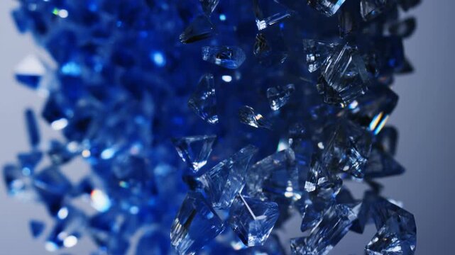 Slow motion macro tracking dolly shot of blue glass shards falling and colliding in midair against gray studio background with controlled lighting