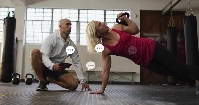 Trainer tapping tablet to prompt client performing side plank kettlebell press for fitness training