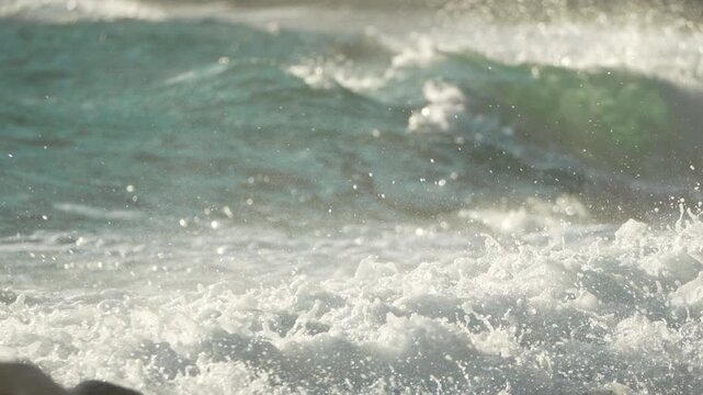 Waves ocean beach, water splashing and foam covering rocks on a sunny day at the shore, bright natural light