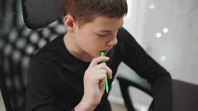 White grandson focused at desk chewing green pen, reviewing notes, mapping ideas, determined expression, modern workspace with mesh chair, daylight bokeh, productive teen study moment