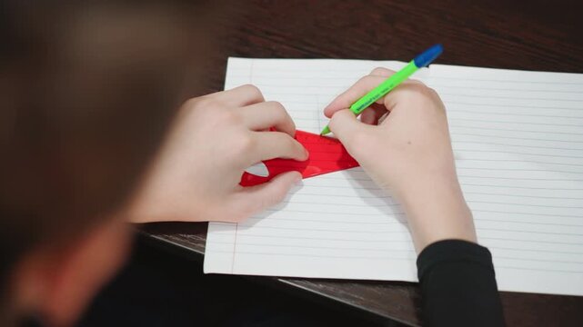 Young boy engaging in detailed writing exercise. Young child focusing on tracing patterns with green pen. Focused grandson carefully copying shapes onto dotted notebook using green pen