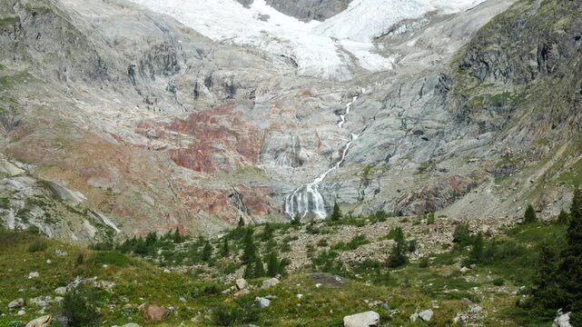 Waterfall generated by a big glacier melting in summer, in Veny Valley, Aosta Valley, Italy. High mountain peak on the background, with blue sky.