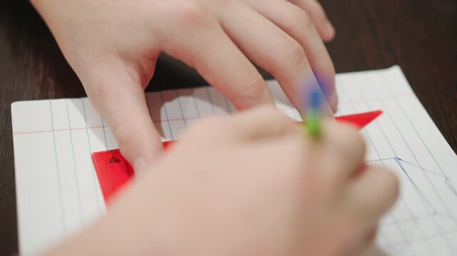 Close up hands drawing with triangle, ruler on lined notebook, steady pencil grip and focused wrist, angles and measurements being traced, student practice session at desk, classroom stationery