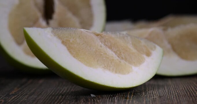 large citrus fruit cut into several pieces with juicy sweet flesh, large citrus fruit cut in half on an old wooden kitchen table, pomelo fruit