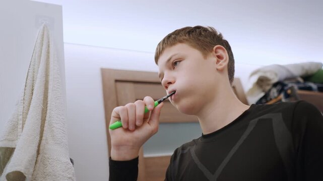 White grandson brushing teeth in bathroom mirror, teenage student prepping for school green brush, towel on hook, natural window light, calm focused expression, closeup angles capturing routine.