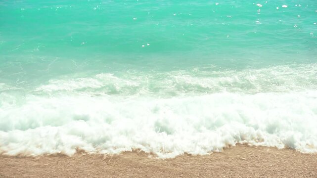 Sea surf. Sunny day on the tropical coast. Waves roll onto the sandy shore. Slow motion. Perfect for travel blogs and travel content.