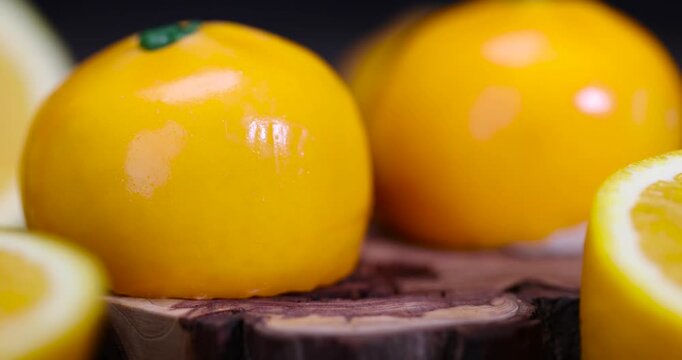 An orange-shaped pastry, a mousse pastry with glossy orange glaze and a green tail next to slices of fresh citrus in a studio with crisp details and an authentic look.