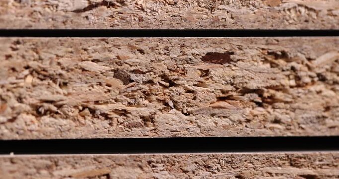 The chipboard panel has a rough edge, a construction panel with a texture of crushed wood and binder in a macro with an authentic look and a natural beige color scheme.