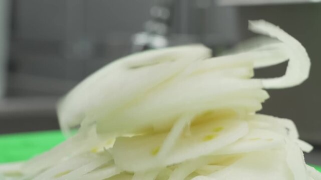 A close-up, high-detail shot of raw, white onion rings piled on a bright green preparation surface, ready for cooking or use as an ingredient.