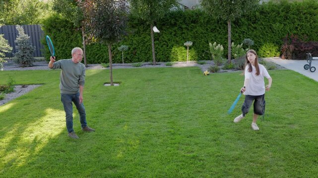 Active Grandfather Playing Racket Game With Granddaughter In Backyard Garden