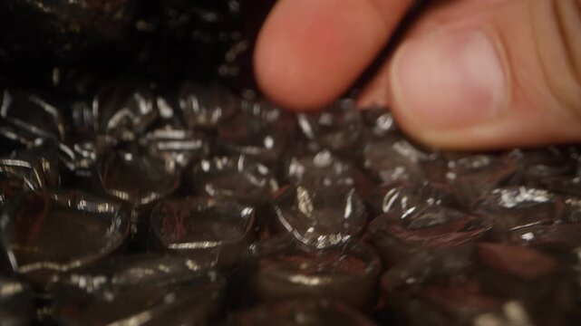 Extreme macro dolly movement showing a hand pressing black bubble wrap and collapsing air bubbles in protective packaging film. Close up cinematic view of plastic packing material under finger pressur