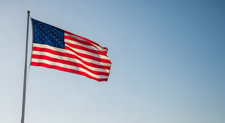 Obraz premium American flag proudly waving against a clear blue sky on a bright and sunny day.