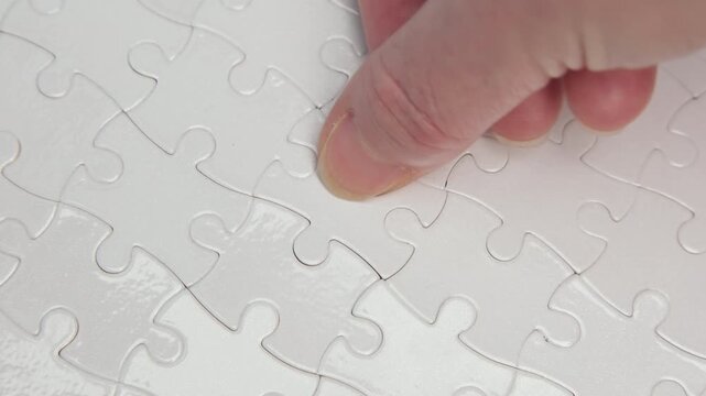 Human hand placing final piece to complete white jigsaw puzzle close-up, solution to assigned tasks, achieving success