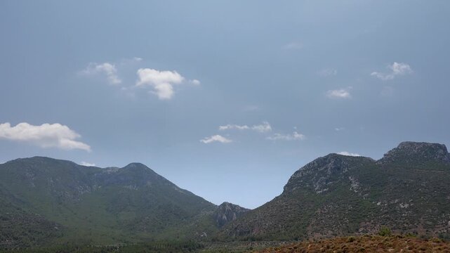 Timelapse clouds drift over Rocky Mountains forest landscape beneath clear blue sky. Fast motion cumulus forming across alpine ridgeline, wooded hillsides, bright daytime air.