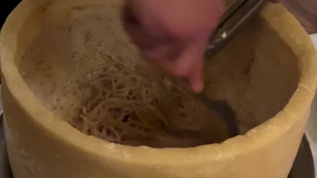 Chef tossing spaghetti inside large parmesan cheese wheel for cacio e pepe preparation