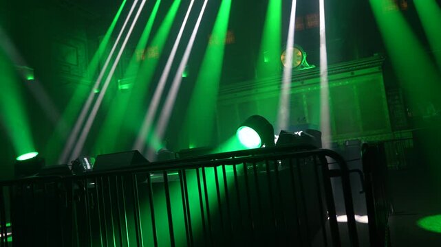 Bright green spotlights cut through the dark atmosphere of an empty stage or venue. The dynamic beams create circular patterns on the floor, evoking an energetic mood for a concert or live event.
