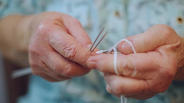 Macro closeup grandma fingers knitting with multiple needles, wrinkled hands manipulating white yarn, precise loops and tension, tactile detail, intimate craftsmanship, soothing repetitive motion