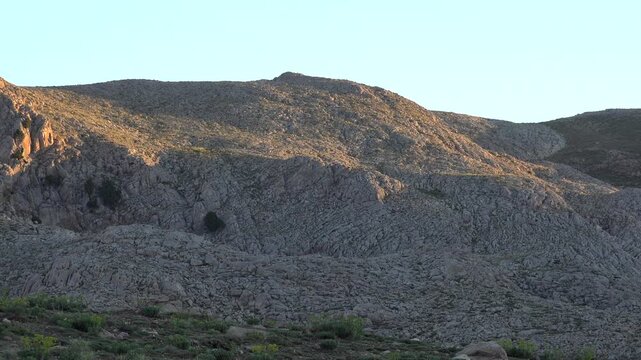 Golden sunrise light sweeps across barren rocky hillside in highland terrain. Warm horizontal rays illuminate treeless slopes of the dry plateau as the camera pans over the silent rugged landscape.