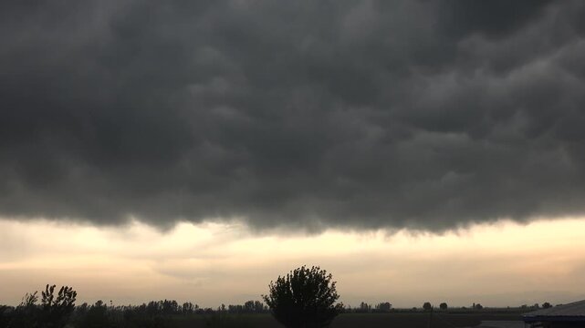 Dark storm clouds advance across a flat plain at dawn with dramatic motion and brooding atmosphere. Ominous overcast masses sweep above open grassland as early light fades before incoming rain.