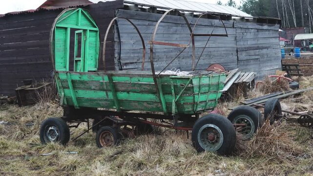 A vintage green wagon sits in a sunny field next to a rustic building