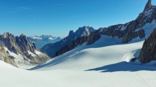 Cinematic aerial view over pristine snowfield framed by dramatic rugged alpine peaks in Chamonix, France. Ideal for travel, winter, nature and adventure themes