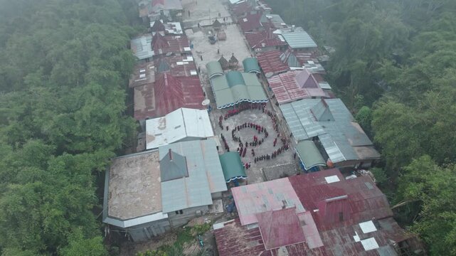 Cinematic drone shot of local people performing the Reba dance in a misty tribal village, capturing the moody and sacred atmosphere of Flores culture.

