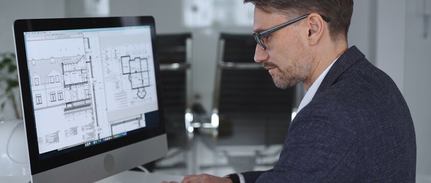 Architect working on computer, analyzing blueprints for new building design and construction planning in office. Business and architecture concept