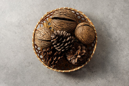 Overhead shot of decorative dried seeds and pine cones in a small bamboo basket on gray stone background, rustic home decor style.