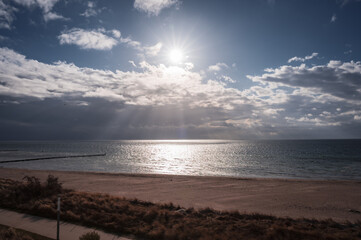 Obraz premium The sun shines through the clouds and illuminates the beach and the sea, the view over the sandy beach to the Baltic Sea, southern beach in 23775 Großenbrode, Germany