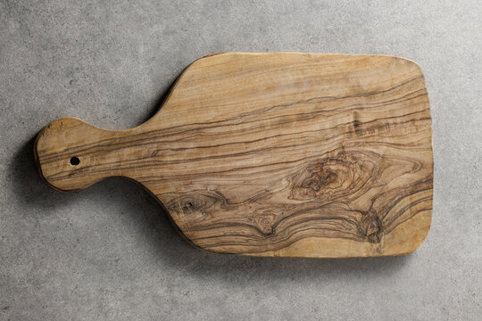 Overhead shot of a textured wooden chopping board with handle, placed on a gray concrete background for culinary design.