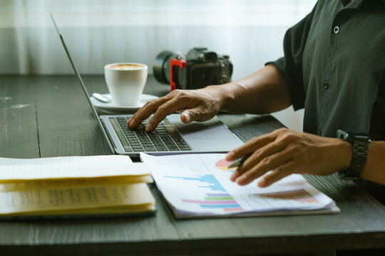 Close up of hands typing on laptop keyboard with business reports and coffee on desk.