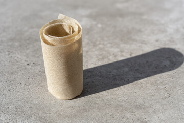 Obraz premium Reusable beeswax food wrap rolled on gray concrete surface with natural sunlight casting shadow, eco friendly alternative for sustainable food storage